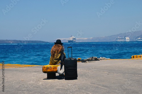 A female tourist waiting for the ferry to depart from a Greek port. A tourist siting on a bench waiting for the ferry to come and pick her up.