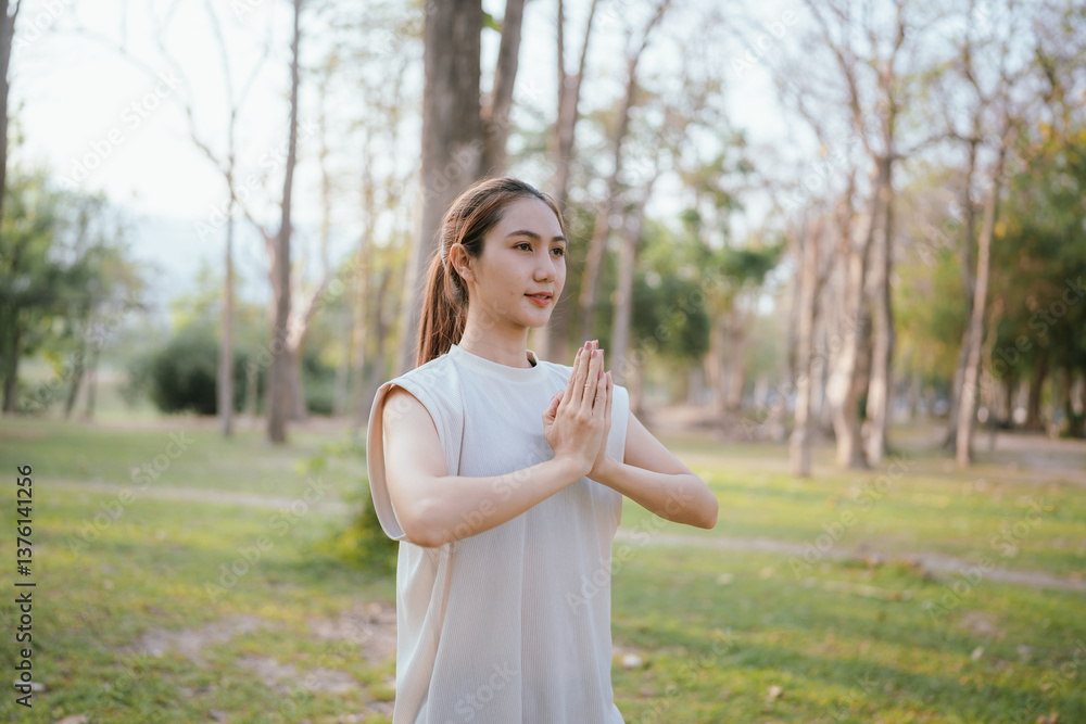 Young Asian woman practicing yoga in a quiet park, gracefully in a relaxed pose, relaxing and strengthening her body, flexibility and relaxation amidst the green grass. Young Asian woman practicing yoga in a quiet park, gracefully in a relaxed pose, relaxing and strengthening her body, flexibility and relaxation amidst the green grass.