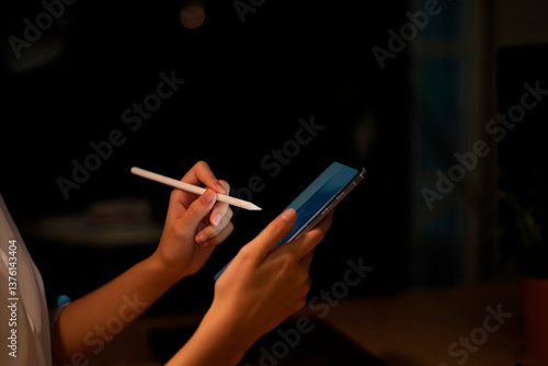 Obraz na płótnie the hands of a woman holding a smartphone. In one hand she holds the phone, and in the other - a stylus or pen
w salonie