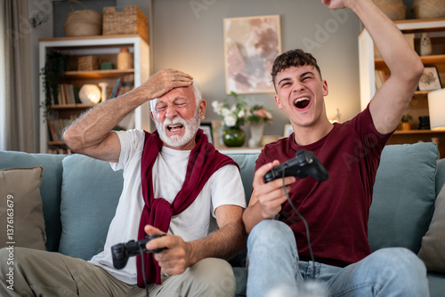 Foto Grandson and grandfather playing videogames on sofa at home: generation gap