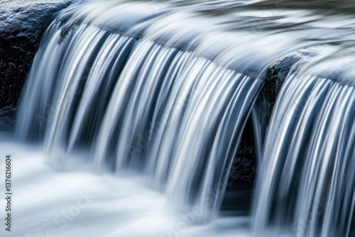 Water cascading over rocks, creating a smooth, flowing curtain of liquid. The scene is peaceful and serene, showcasing nature's beauty.