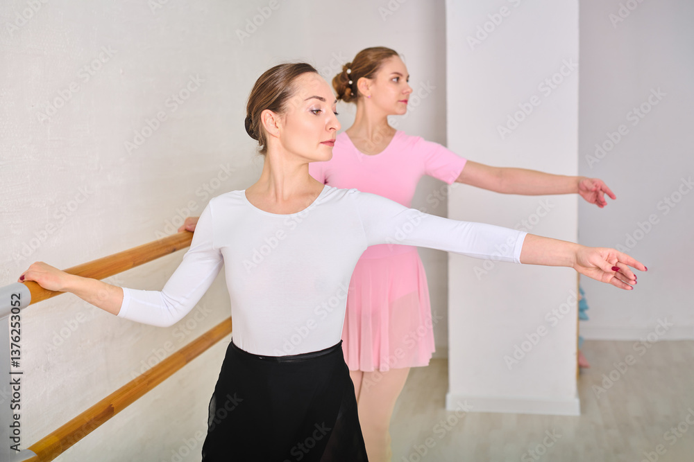 Fototapeta premium Young female ballerinas rehearsing at ballet barre in bright studio
