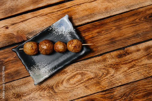 Shish kebab made from small young round grilled potatoes with a baked skin on a brown wooden background.