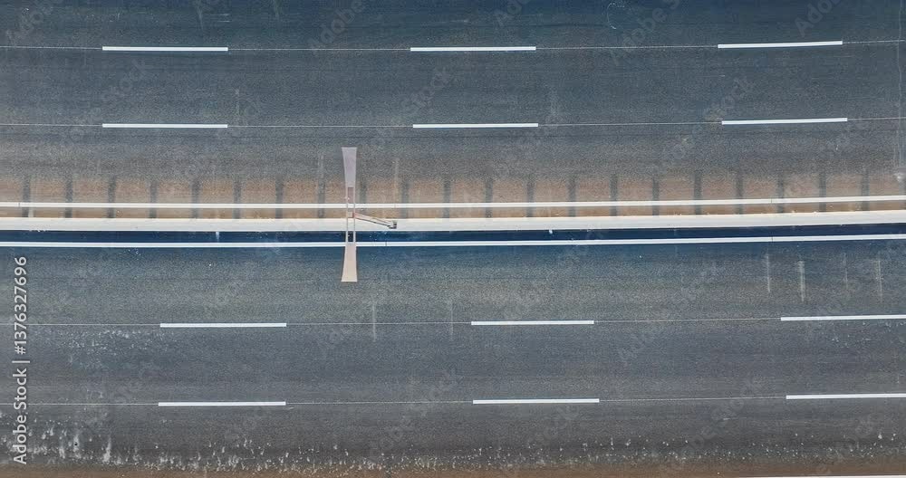 Aerial view of asphalt road with white lane markings and median. Transportation infrastructure and travel background. Aerial view of asphalt road with white lane markings and median. Transportation infrastructure and travel background.