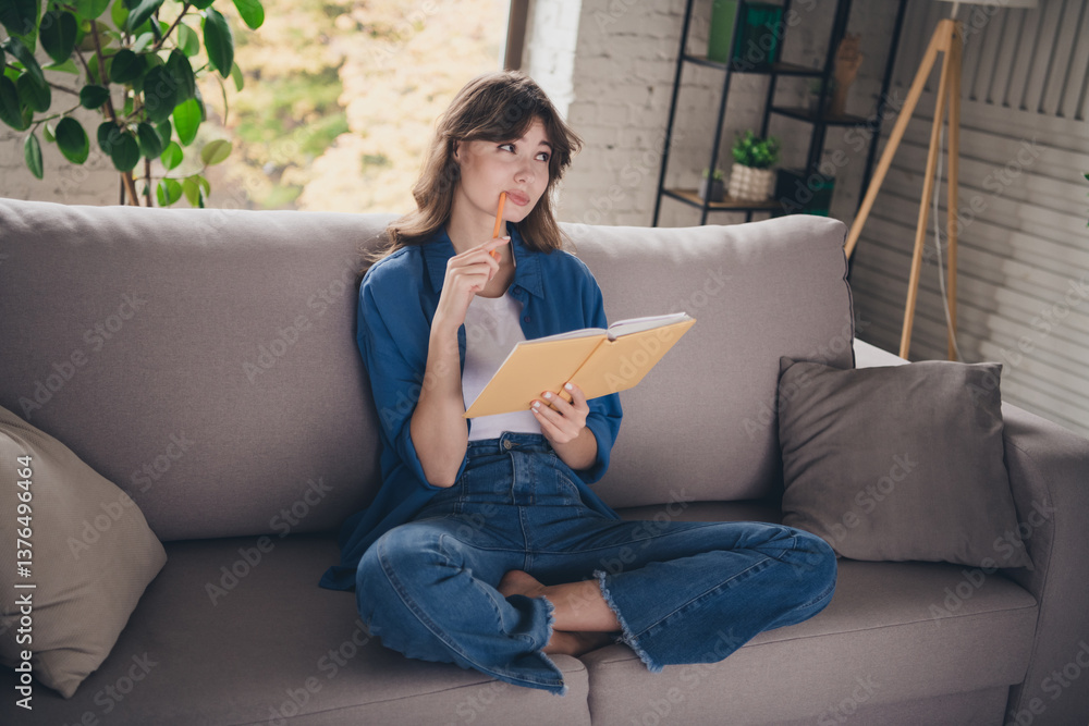Young woman sitting on a couch reading a notebook during a relaxing afternoon at home Young woman sitting on a couch reading a notebook during a relaxing afternoon at home