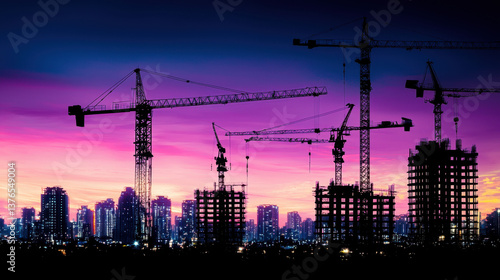 Silhouetted Construction Cranes at Sunset Over City Skyline