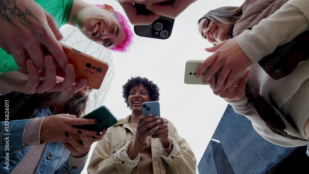 Low angle view of young group of people using mobile phones together at city street. Diverse college student friends watching social media content on cell. Cellphone addicted people concept.