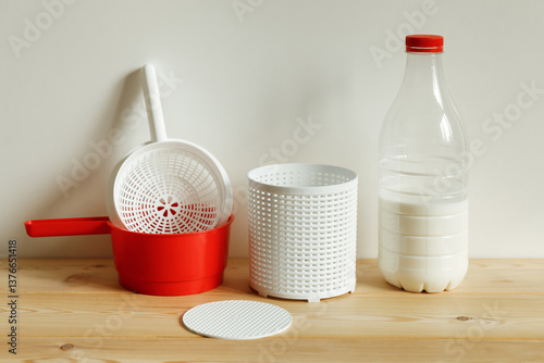 Plastic equipment for making soft cheese and cottage cheese at home. A white uniform, a red ladle and a bottle of milk.