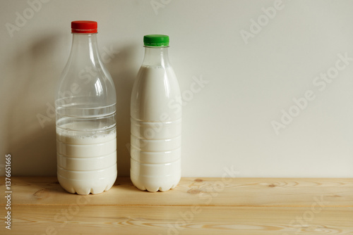 Two transparent plastic milk bottles on the table on a light monochrome background.