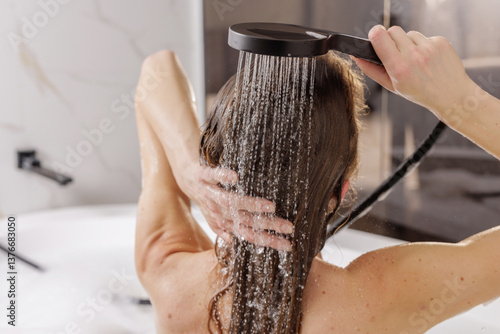 Woman rinsing long hair with shower, luxurious spa beauty and haircare routine in home bathtub.