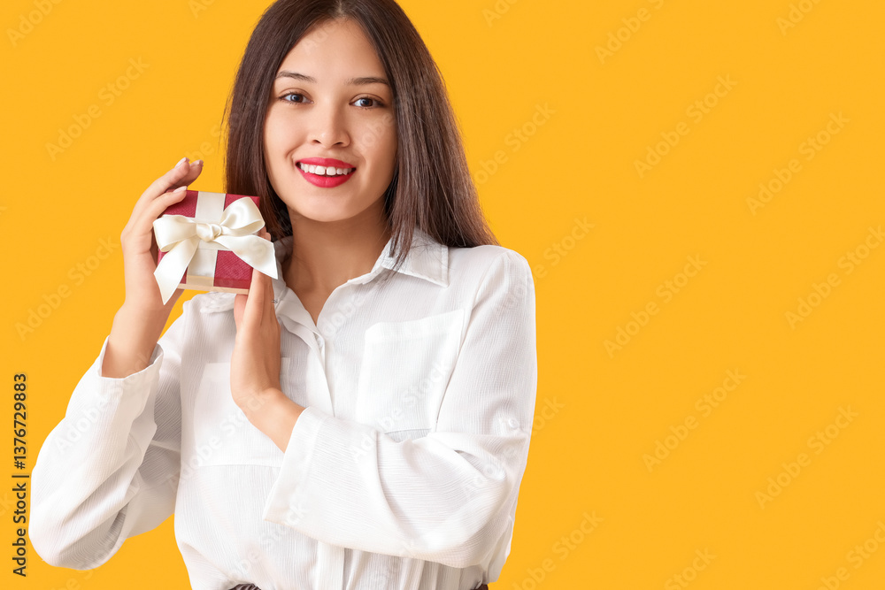 Beautiful young Asian woman with gift box on yellow background Beautiful young Asian woman with gift box on yellow background