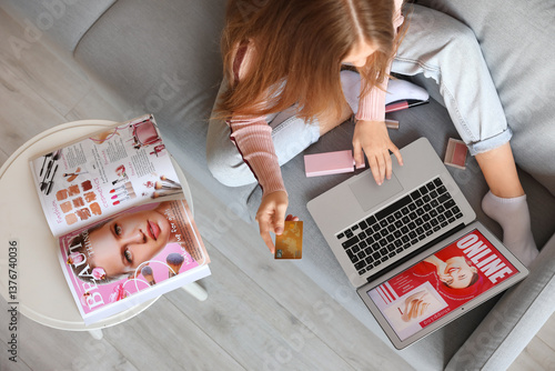 Woman with credit card and makeup products shopping online on sofa at home, t...