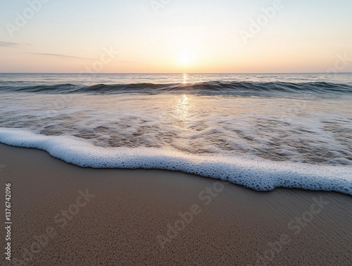 Sunrise over the calm ocean waves at a sandy beach with gentle foam on the shore