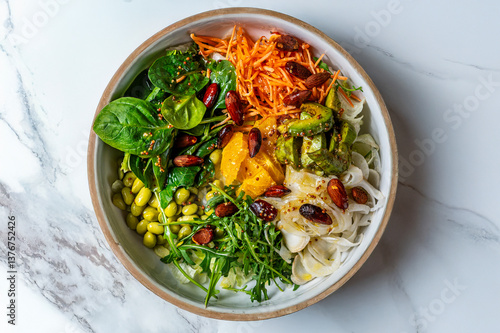 Vegetarian bowl with orange, avocado, salad, fennel, carrots, edamame, rocket and roasted almonds on a marble background. Fresh and colourful dish, minimal and modern style, perfect for a healthy meal
