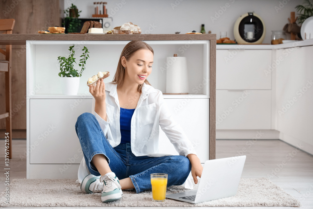 Young happy woman holding laptop, glass of juice and tasty toast with fresh butter in kitchen at home Young happy woman holding laptop, glass of juice and tasty toast with fresh butter in kitchen at home