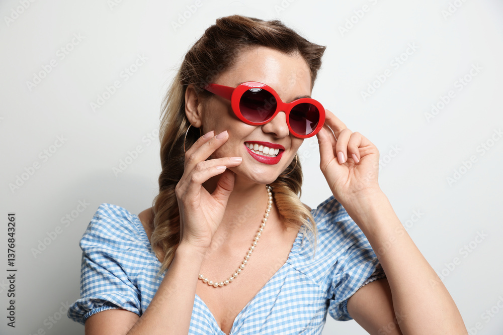 Naklejka premium Portrait of happy pin-up woman in sunglasses on light background