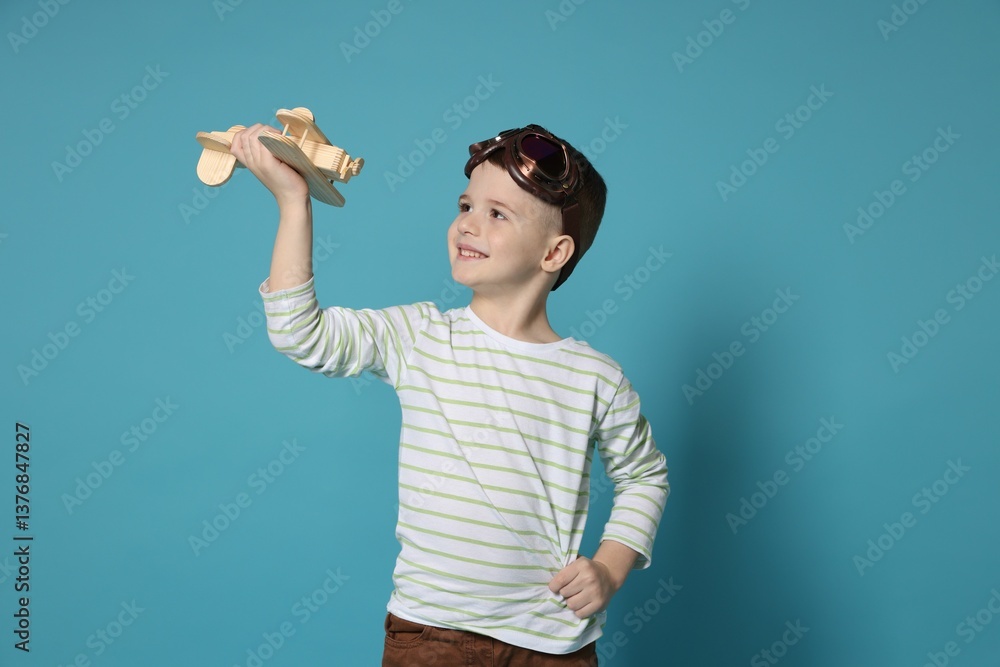 Happy little boy playing with toy plane on light blue background Happy little boy playing with toy plane on light blue background