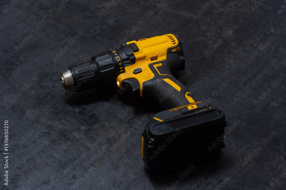 Yellow cordless drill rests on a dark textured surface. Powerful tool for construction and DIY projects. Yellow cordless drill rests on a dark textured surface. Powerful tool for construction and DIY projects.
