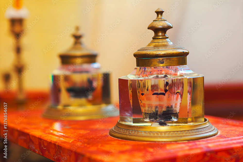 Elegant antique inkwells with brass lids and crystal bodies sit on polished wooden desk, reflecting ambient light. Intricate design and historical charm make it perfect for vintage projects and decor