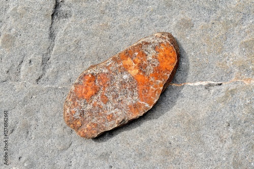 Small Orange Rock on Large Gray Stone Surface. Outdoor closeup