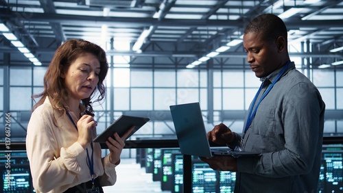 System administrators using notebook device in data center, managing server virtualization. IT specialists using laptop in server farm, sustaining long term infrastructure reliability, camera B