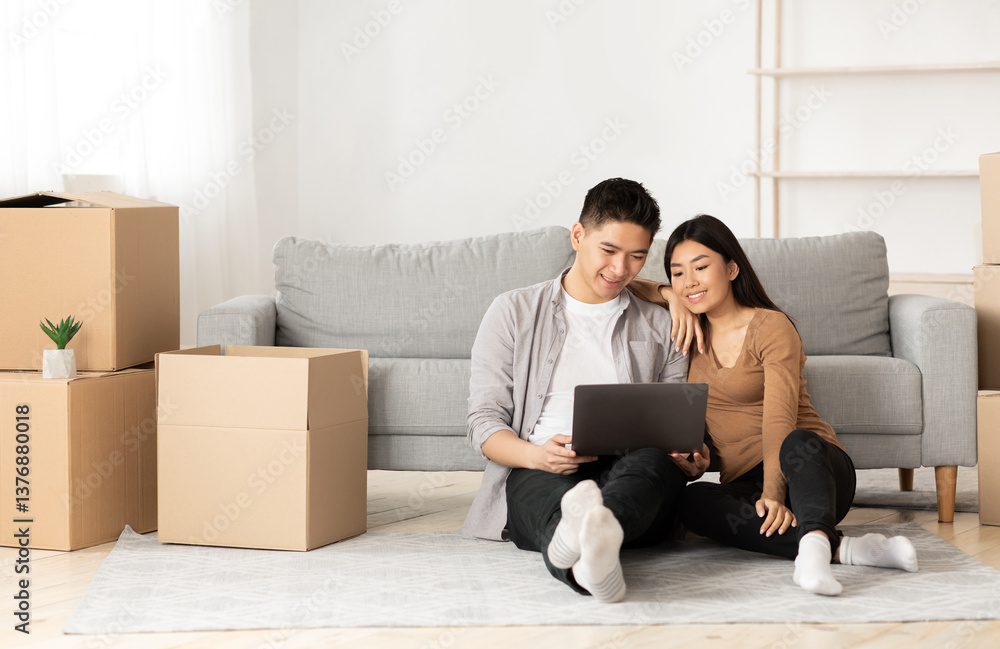 Online Ordering Concept. Asian family using laptop sitting on floor among boxes, empty space Online Ordering Concept. Asian family using laptop sitting on floor among boxes, empty space