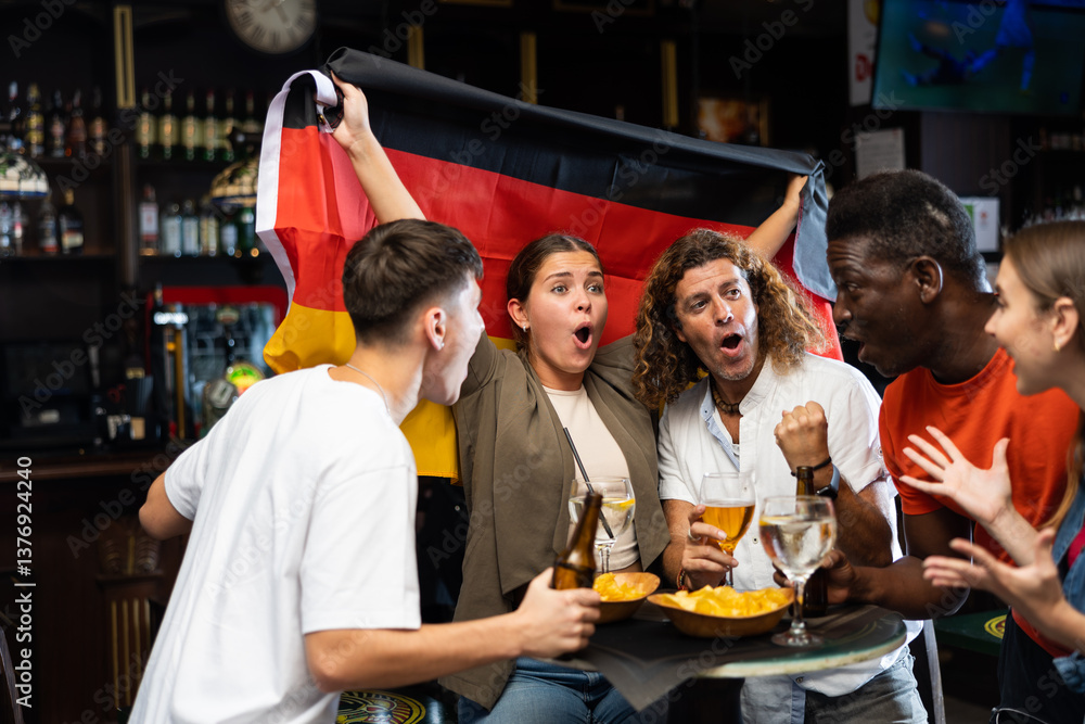 Diverse men and women supporting Germany sports team in pub together. Happy group of friends raising German flag. Diverse men and women supporting Germany sports team in pub together. Happy group of friends raising German flag.