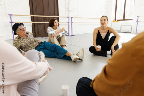 Professional dancer sitting on floor and talking to group of retirees 