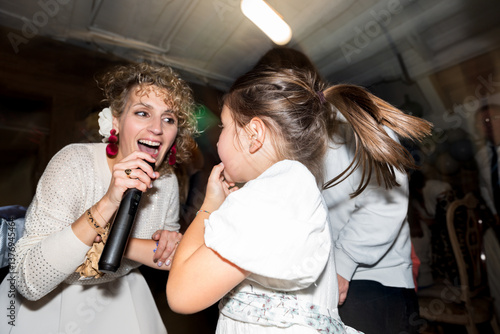 Woman singing with microphone and little girl dancing at party
