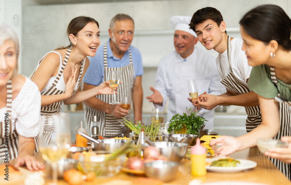 Cheerful learners of culinary classes engaged in spirited conversation around kitchen table while learning cooking fish Cheerful learners of culinary classes engaged in spirited conversation around kitchen table while learning cooking fish