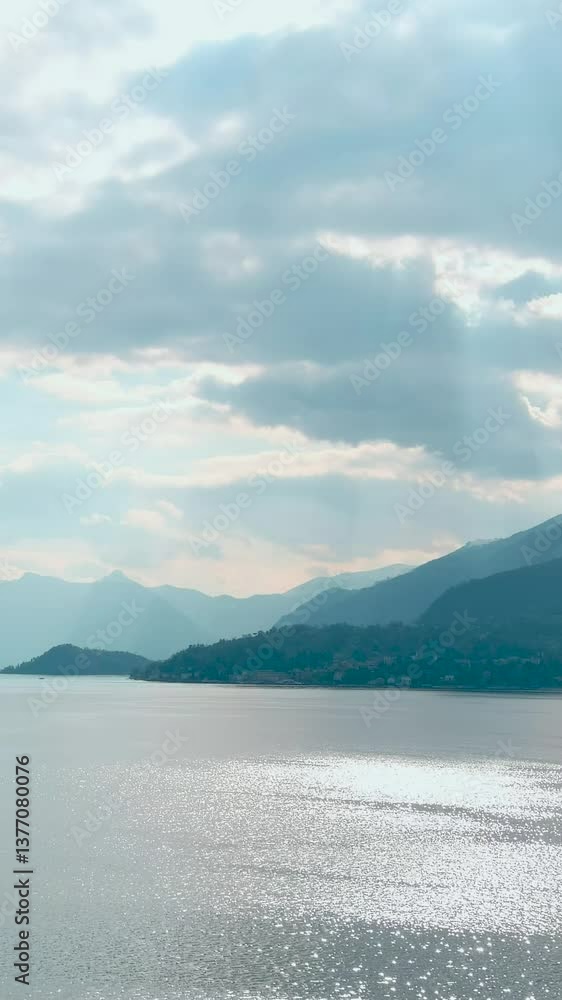 Lago di Como. Aerial vertical view of great lake Como waters, vicinity of Varenna. Fresh air, clouds along the horizon, mountain skyline, picturesque fishing villages. Famous tourist region. Italy Lago di Como. Aerial vertical view of great lake Como waters, vicinity of Varenna. Fresh air, clouds along the horizon, mountain skyline, picturesque fishing villages. Famous tourist region. Italy