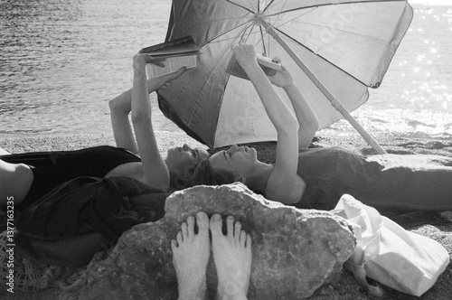 Two Young women reading books on the beach under a sun umbrella