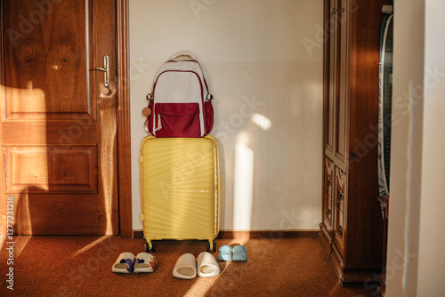 Shoes stand near the front door next to a suitcase and backpack.