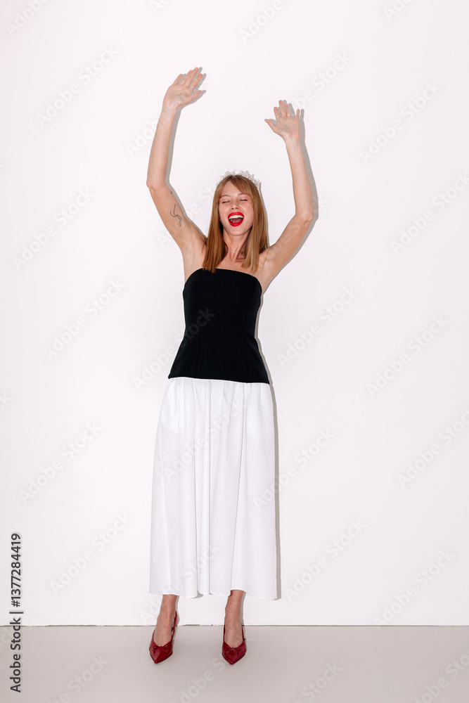 Model poses joyfully with arms raised while wearing a party dress Model poses joyfully with arms raised while wearing a party dress