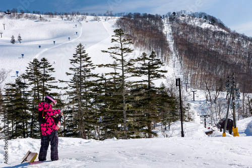 Single female snowboarder at the top of a ski slope on sunny day