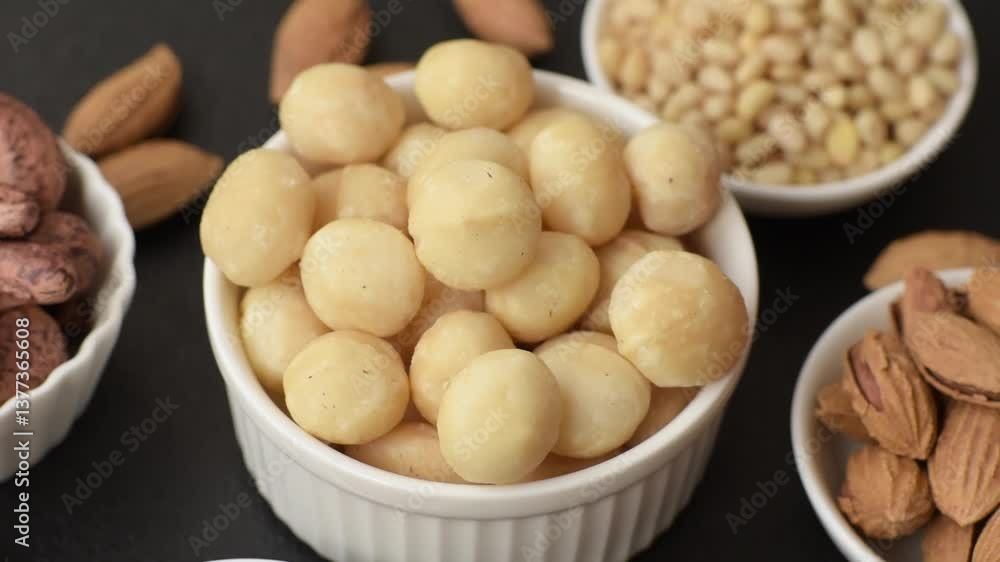 Raw peeled macadamia nut in ceramic bowl on dark concrete background. Nuts as a source of nutrients Raw peeled macadamia nut in ceramic bowl on dark concrete background. Nuts as a source of nutrients