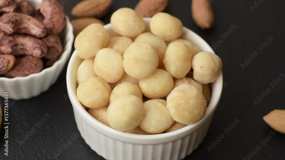 Raw peeled macadamia nut in ceramic bowl on dark concrete background. Nuts as a source of nutrients Raw peeled macadamia nut in ceramic bowl on dark concrete background. Nuts as a source of nutrients