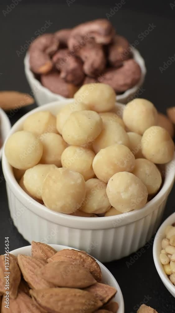 Raw peeled macadamia nut in ceramic bowl on dark concrete background. Nuts as a source of nutrients Raw peeled macadamia nut in ceramic bowl on dark concrete background. Nuts as a source of nutrients