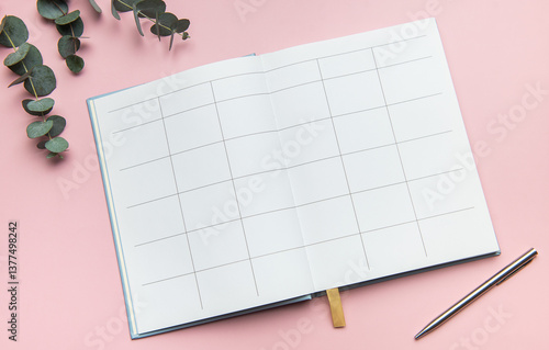 Open notebook showing blank pages with pen and eucalyptus leaves on pink background