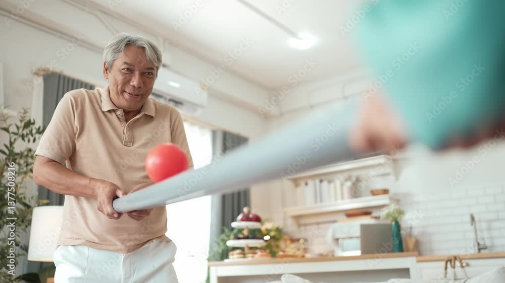 Elderly man playing a ball rolling game with his partner at home, practicing hand-eye coordination, focus, and motor skills for mental and physical wellness. Preventing healthcare concept. Myrmidon. Elderly man playing a ball rolling game with his partner at home, practicing hand-eye coordination, focus, and motor skills for mental and physical wellness. Preventing healthcare concept. Myrmidon.