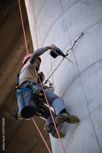 Rope access technician using drill while hanging on concrete pillar