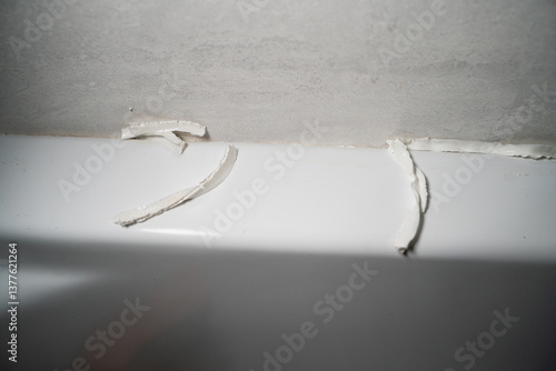 Poor quality white sealant in shower stall close-up. Removing sealant to replace and applying fresh sealant to protect against moisture