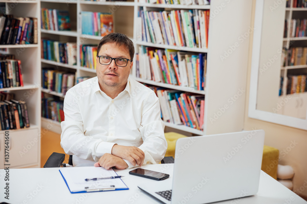 Man working learning at desk with laptop in library with books Man working learning at desk with laptop in library with books
