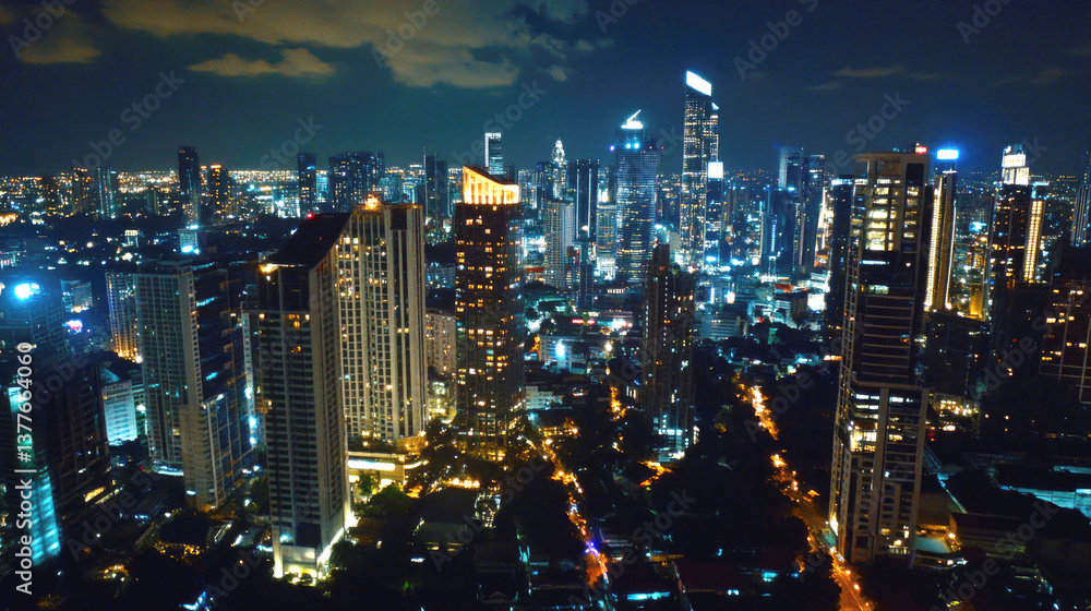 Fototapeta premium Captivating nighttime aerial cityscape with illuminated skyscrapers and cloudy sky