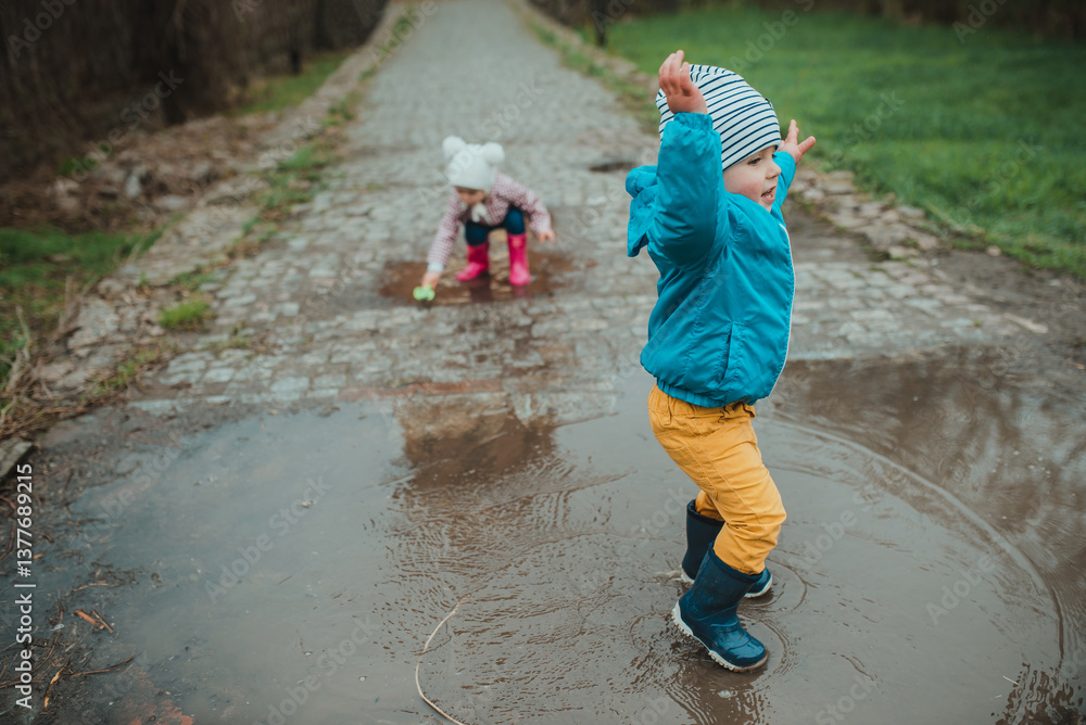 Three children playing in a puddle in spring. Walks in rainy weather. Strengthening immunity and hardening, early development. Kindergarten activities and walks in the fresh air Three children playing in a puddle in spring. Walks in rainy weather. Strengthening immunity and hardening, early development. Kindergarten activities and walks in the fresh air