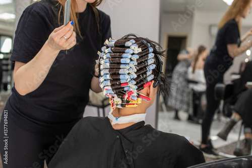 Hairdresser winding perm rods. Woman is getting her hair done by a stylist. The stylist is using a comb to style the woman's hair.