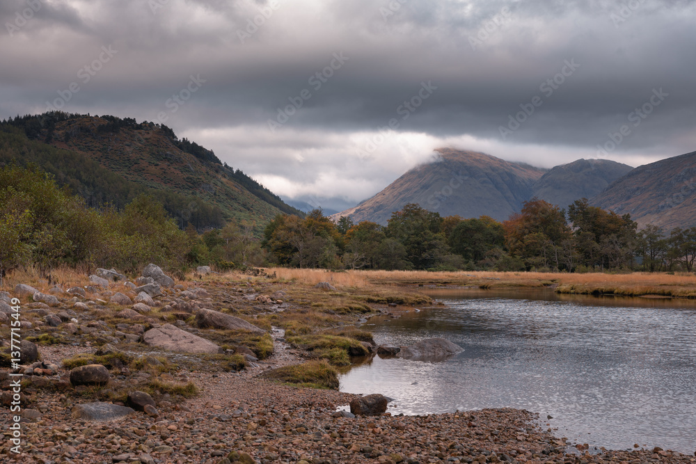 Dramatic peaks and misty valleys define Glen Coe, Scotland’s iconic Highland landscape. Golden light dances on rugged slopes, creating a scene of wild, untamed beauty.