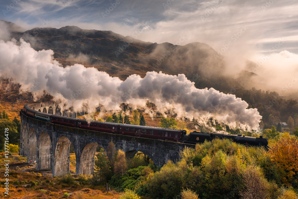 The morning train steams across the Glenfinnan Viaduct, its plume rising against the Highland mist. Golden light touches the hills, creating a scene of timeless beauty in Scotland’s heart.