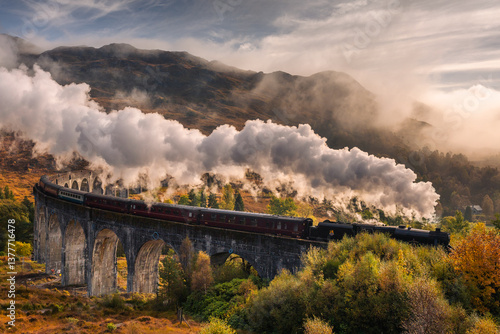 Obraz na płótnie The morning train steams across the Glenfinnan Viaduct, its plume rising against the Highland mist. Golden light touches the hills, creating a scene of timeless beauty in Scotland’s heart. w salonie