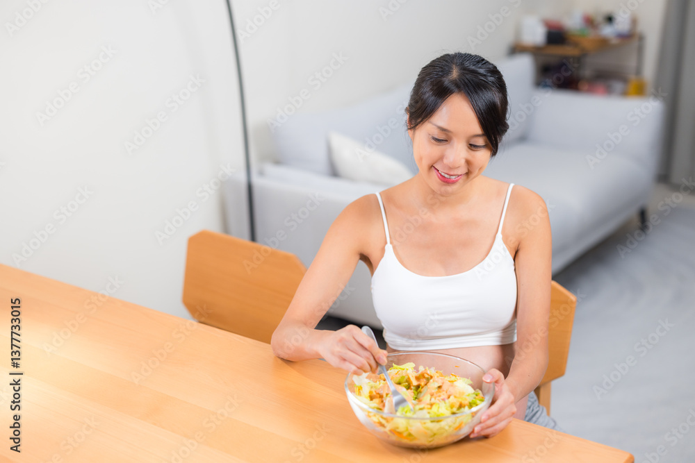 Pregnant woman eating fresh salad at home in daytime